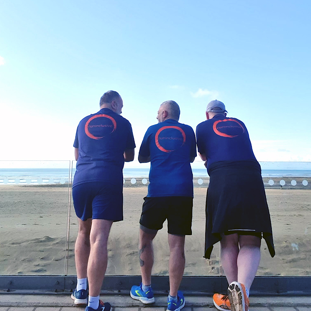 The 3 amigos at the beach, wearing blue runinclusive t-shirts, looking out towards the sea